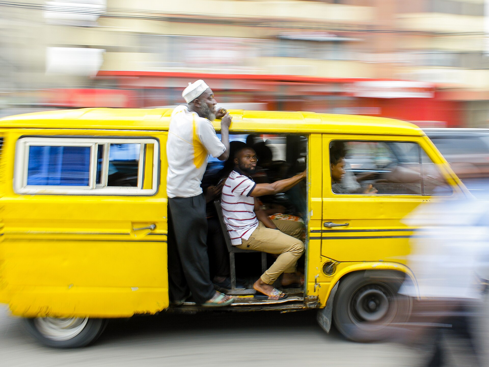 A yellow Danfo bus carrying passengers through a street in Ikeja, Lagos
